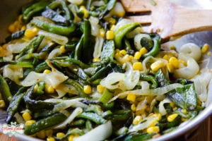 Rajas con elote y cebolla en una caserola con una cuchara de madera