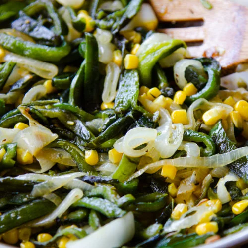 rajas con elote y cebolla en una caserola con una cuchara de madera