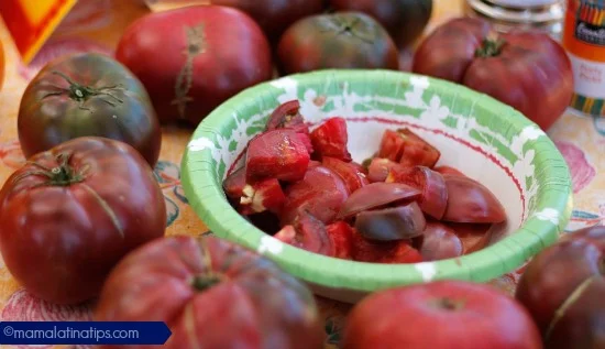 Eight Heirloom Tomatoes Purple Cherokee placed in a circle, in the middle there is a bowl with chopped tomatoes.