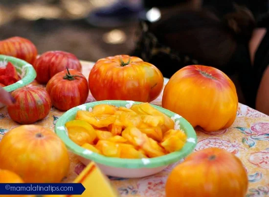 Four whole Heirloom tomatoes golden jubilee and a few chopped in a bowl on top of a table