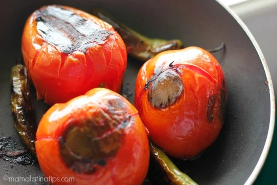 Three charred tomatoes and three charred serrano peppers on a black skillet.