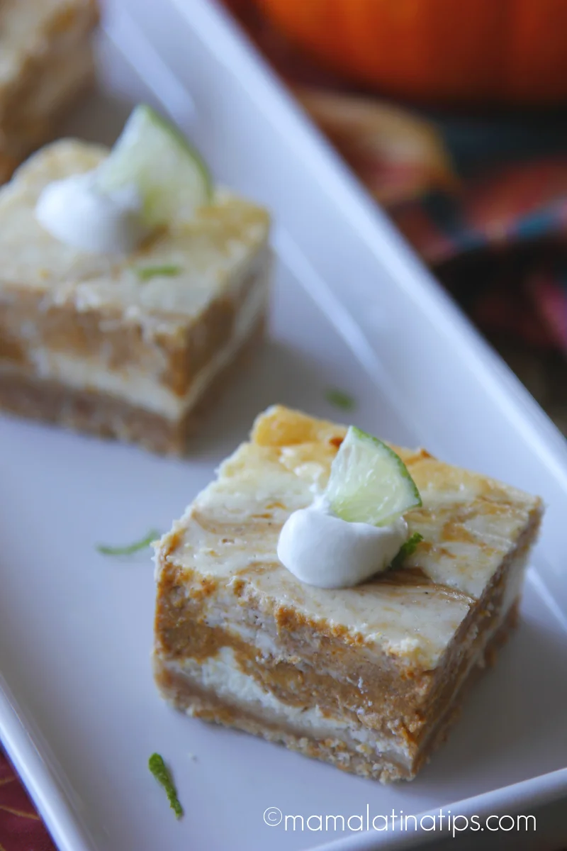 Una barra cuadrada de queso crema marmoleada con calabaza de castilla adornada con crema batida y un pedacito de limón.