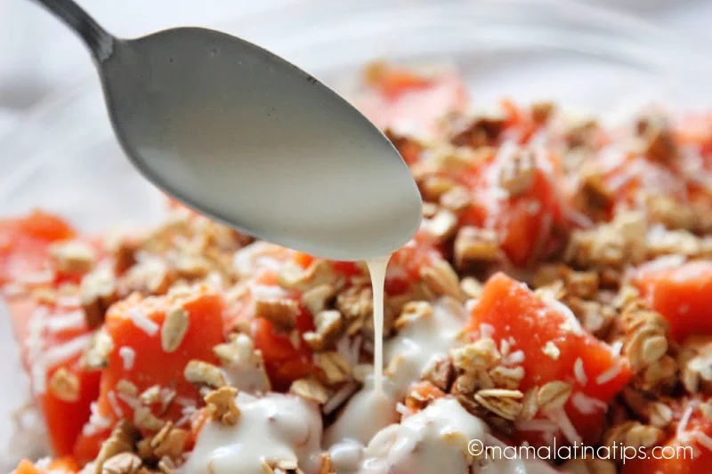Pouring yogurt on top of chopped papaya with granola
