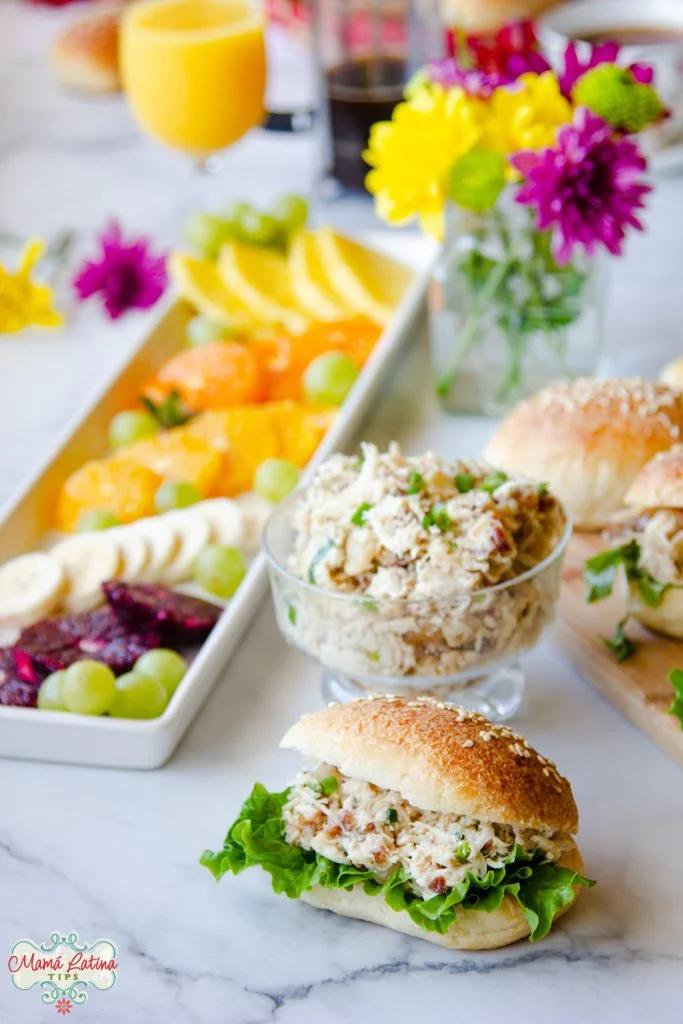 Un sandwich relleno de ensalada de pollo y lechuga junto a un recipiente con más ensalada y otra ensalada de frutas.