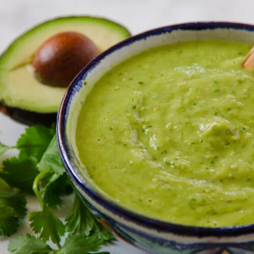 salsa de aguacate en una salsera junto a cilantro fresco y medio aguacate