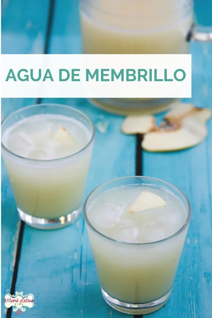 Vasos de refrescante agua de membrillo con hielo descansan sobre una mesa de madera azul, mientras que la fruta en rodajas añade un toque vibrante al fondo.